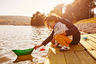 Parent and child pushing a paper boat on a lake